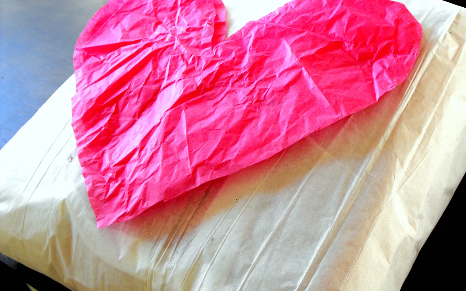 Large pink tissue paper heart covered in wrinkles and creases, lying on a cream paper-wrapped package