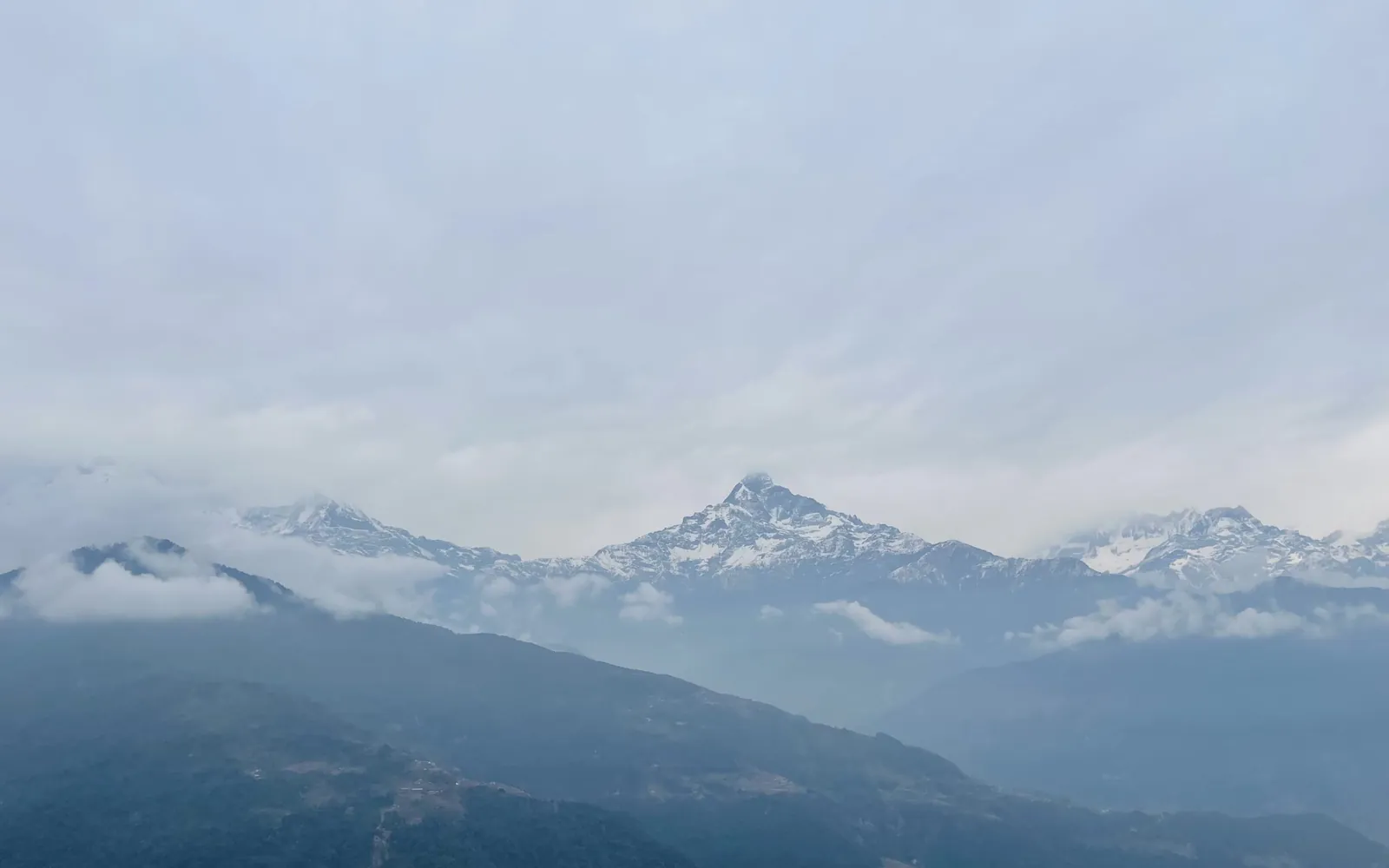 Layers of misty mountain ridges fading into the distance below snow-capped peaks